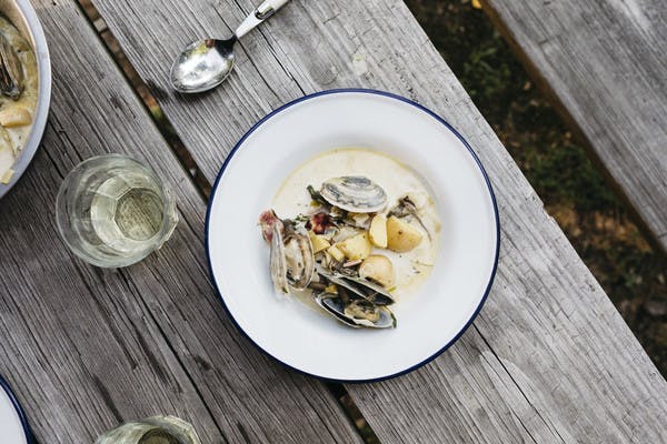 A bowl of freshly made clam chowder on a rustic picnic table outside.