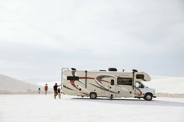 Family of four walking around large Class C motorhome at White Sands in New Mexico.