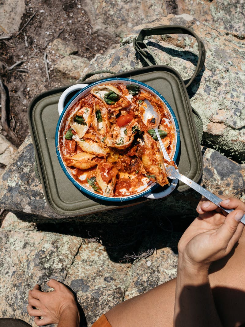 Pasta shells with ricotta cheese, tomatoes, and basil, in a round pan, with a large spoon.