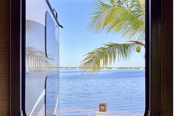 Window To The World Dutchmen Kodiak RV view looking out to the ocean with a palm tree in Key West, Florida.