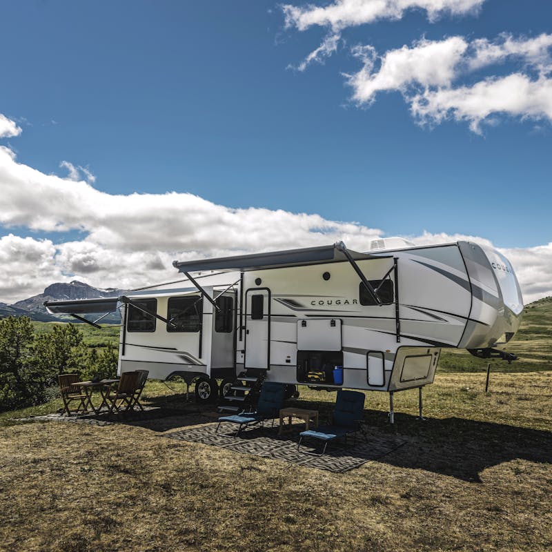 A Keystone Cougar boondocking in a grassy field surrounded by mountains.