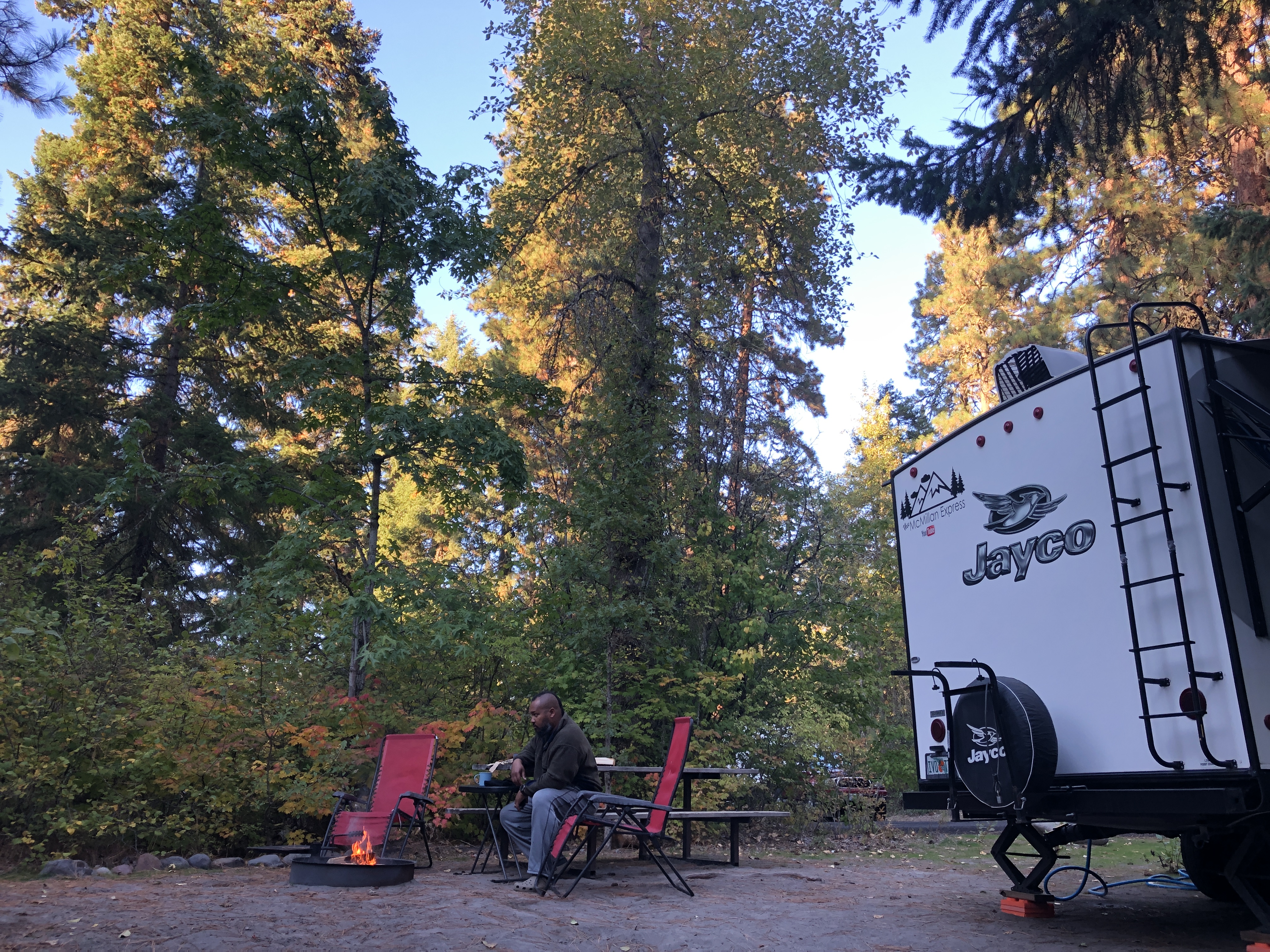 Ben McMillan sits by a campfire next to his Jayco RV