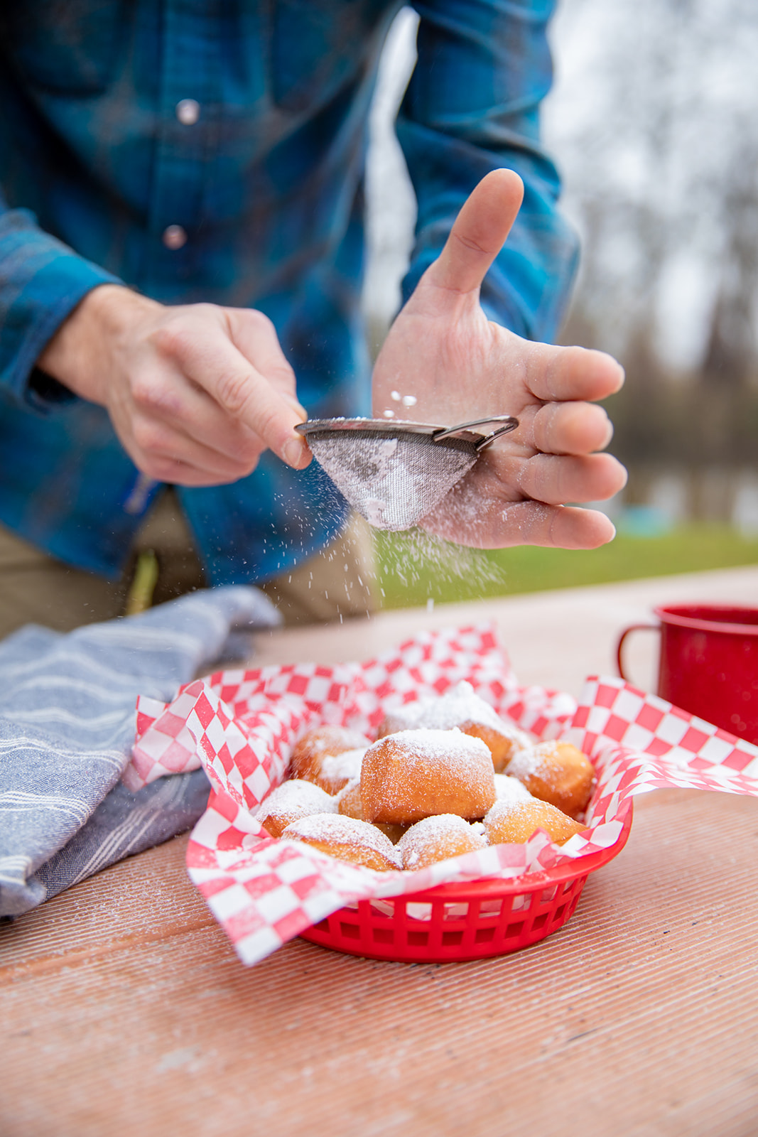 Dusting flour over a basket of fresh beignets. 