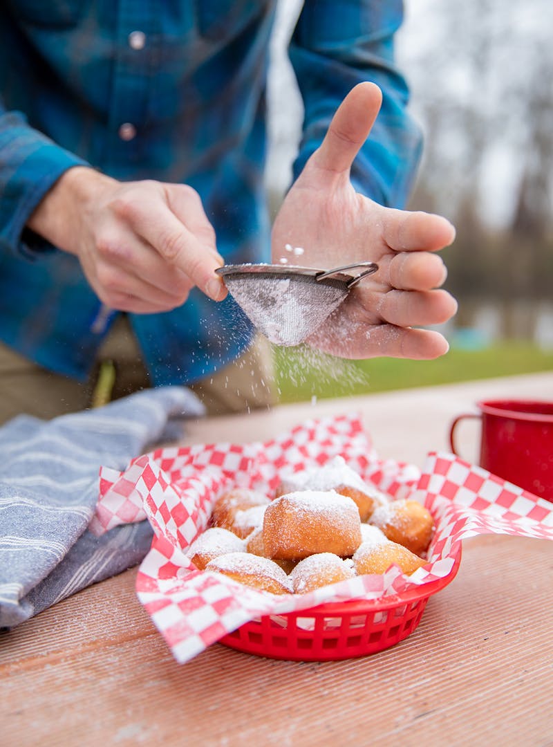 Dusting flour over a basket of fresh beignets.