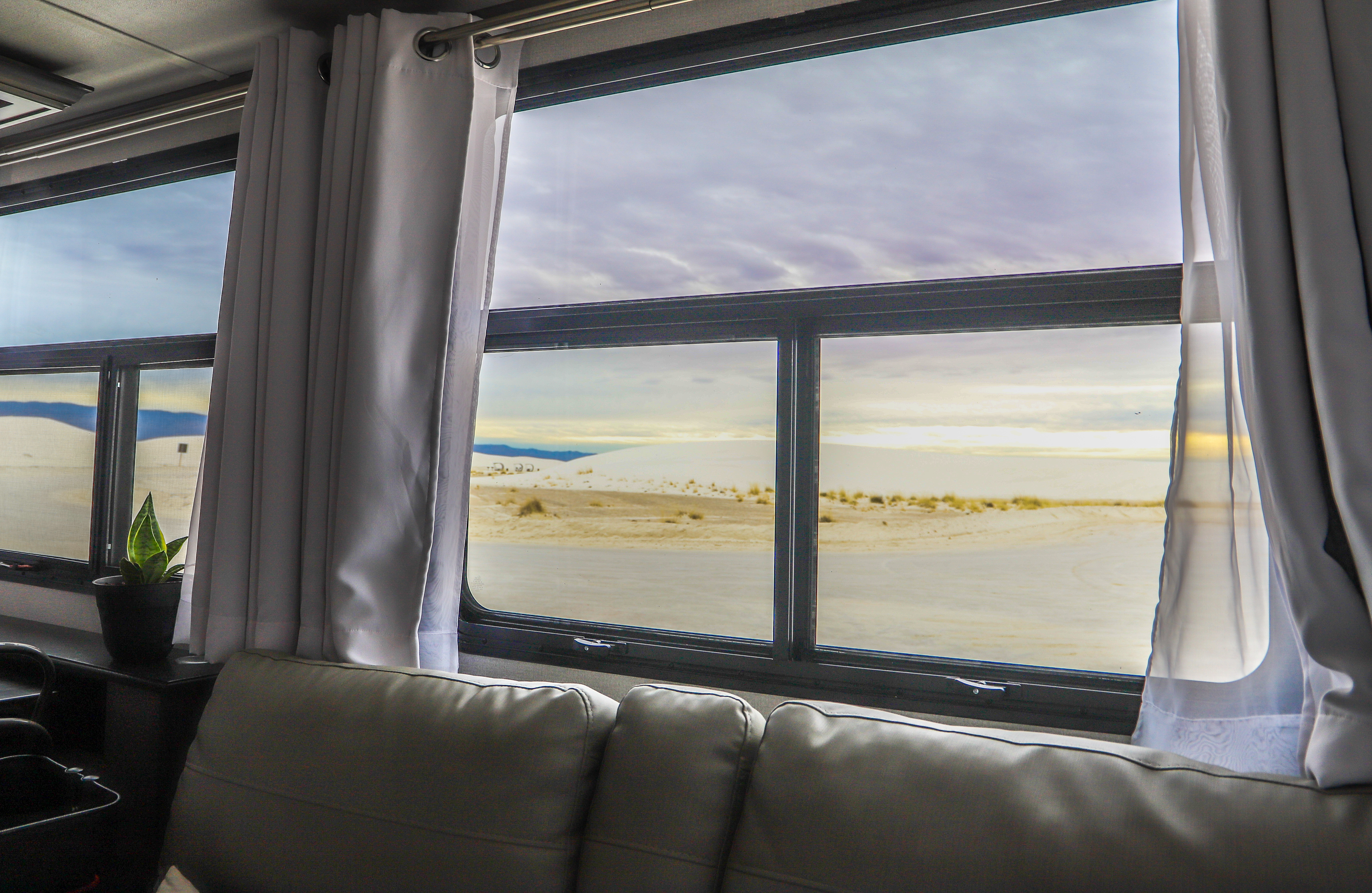 A view out an RV window to the sun setting over white sand dunes. 