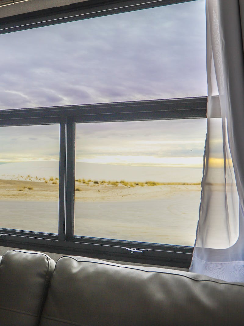 A view out an RV window to the sun setting over white sand dunes. 