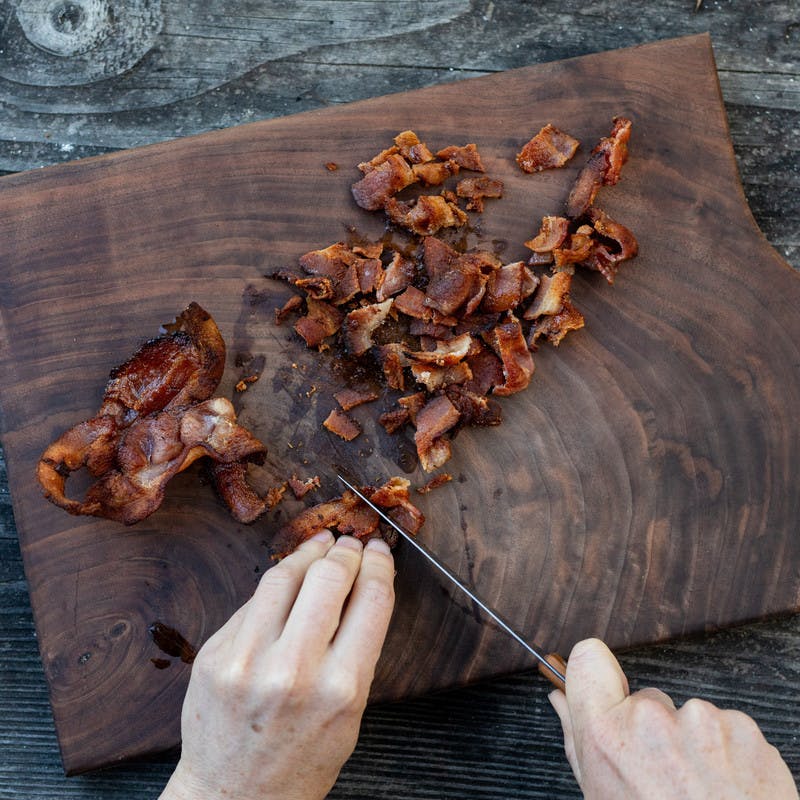 Woman cutting crispy bacon with a knife on a cutting board.