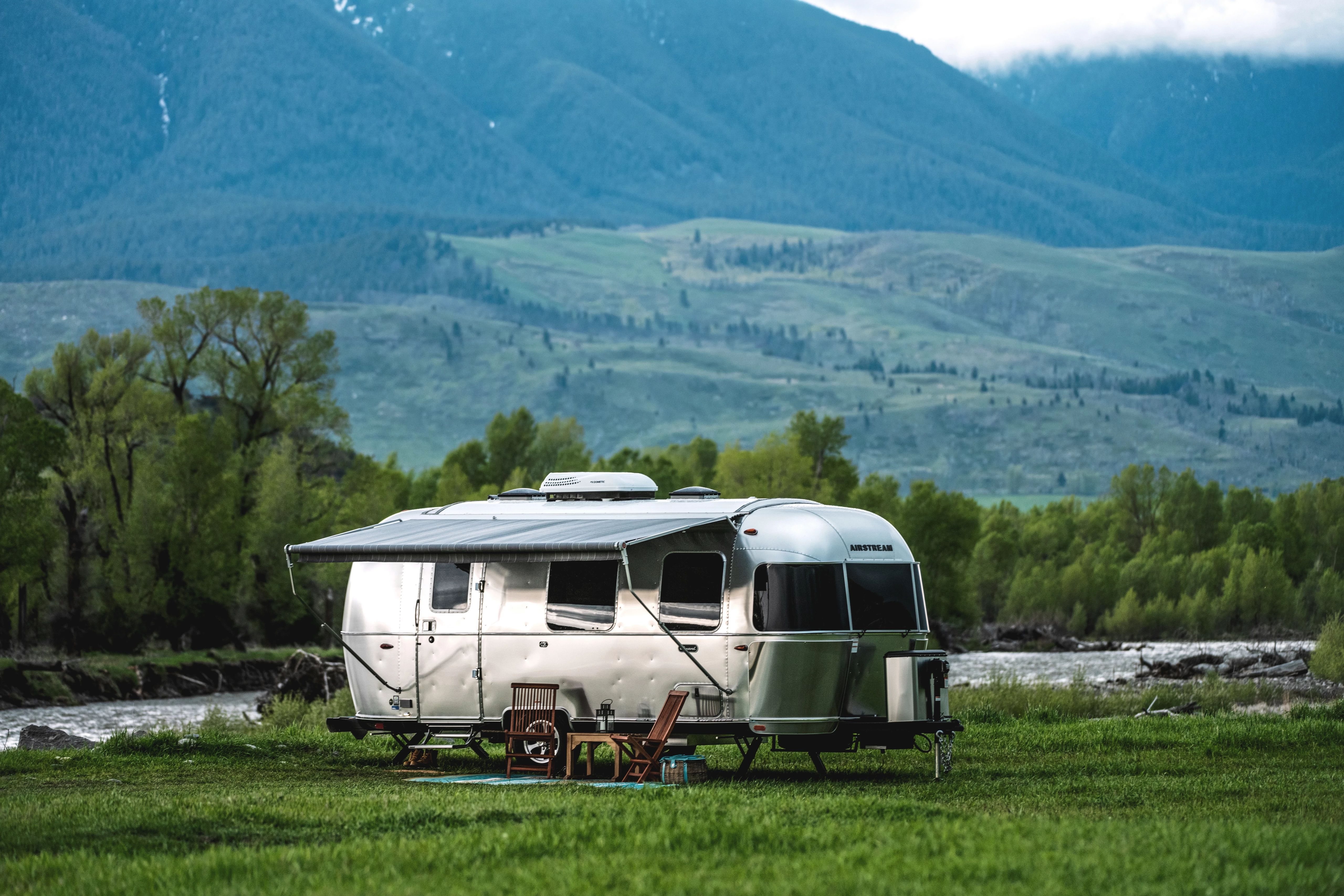 An Airstream Caravel Travel Trailer boondocking by a river near mountains in Montana 