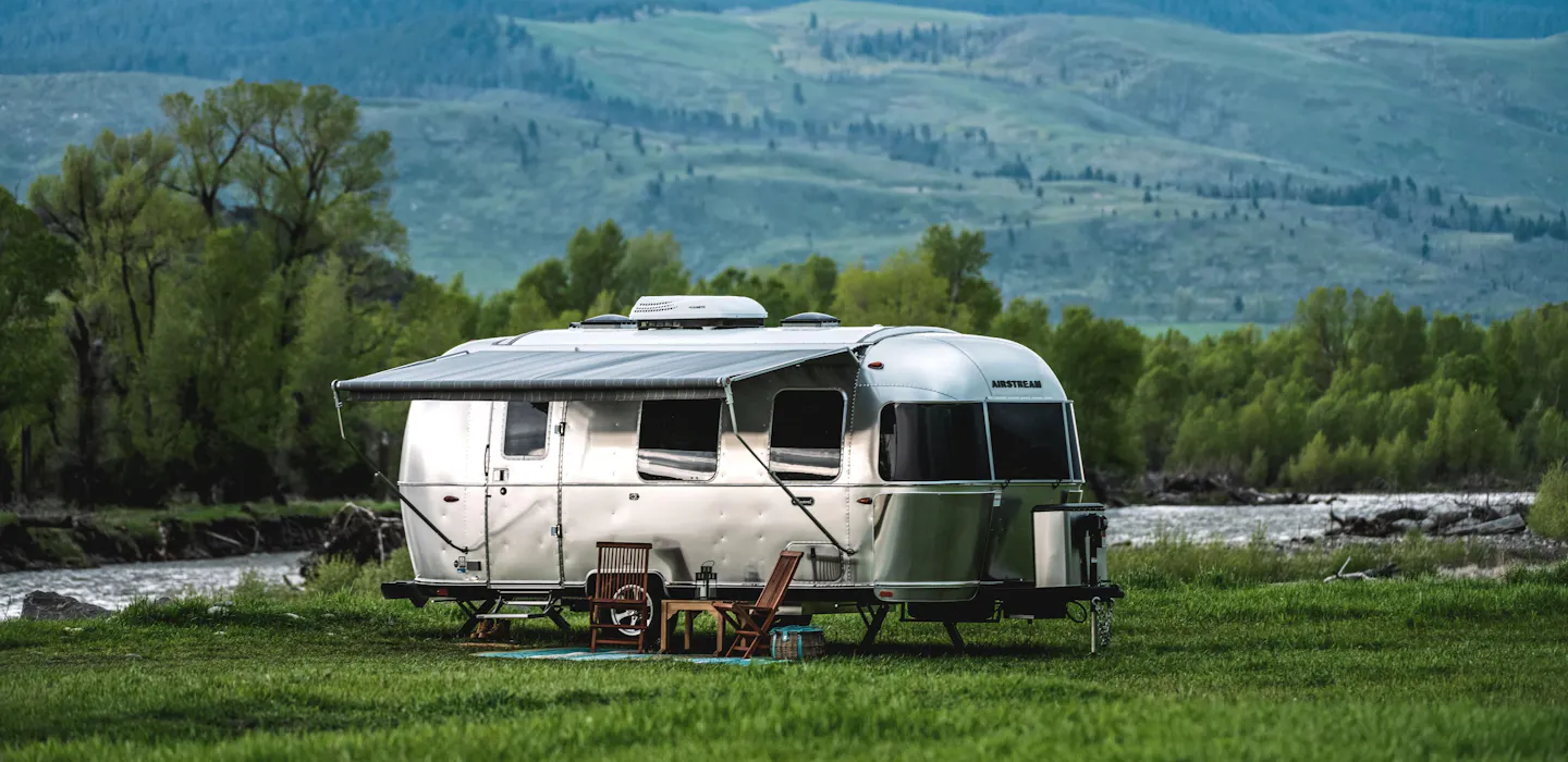 An Airstream Caravel Travel Trailer boondocking by a river near mountains in Montana 