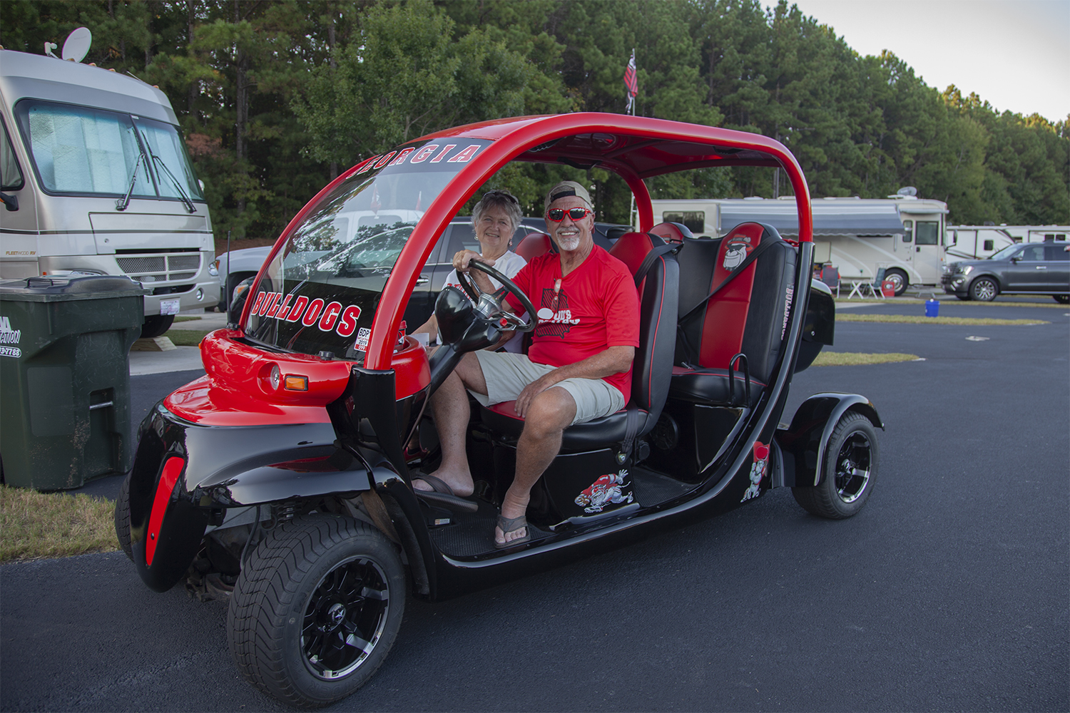 An older man and a woman inside a tricked-out red golf cart, perfect for tailgating. 