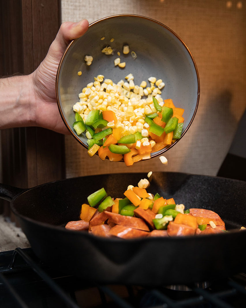 Pouring corn, green and red peppers into a skillet. 