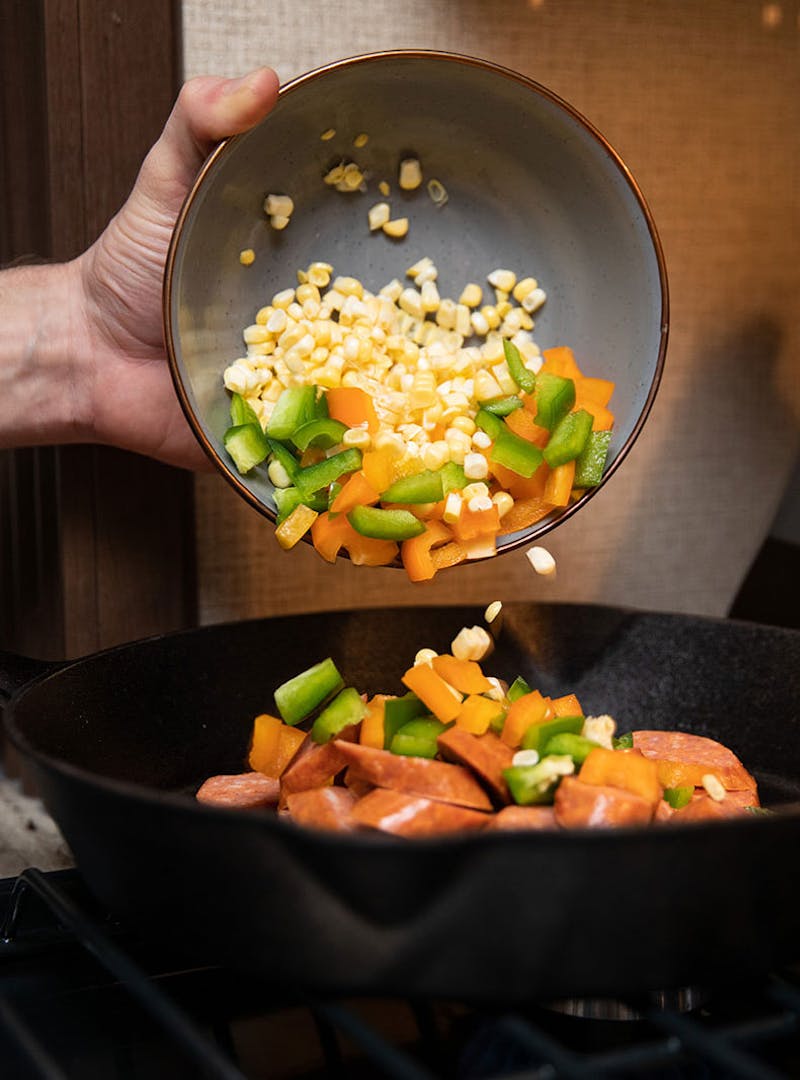 Pouring corn, green and red peppers into a skillet.