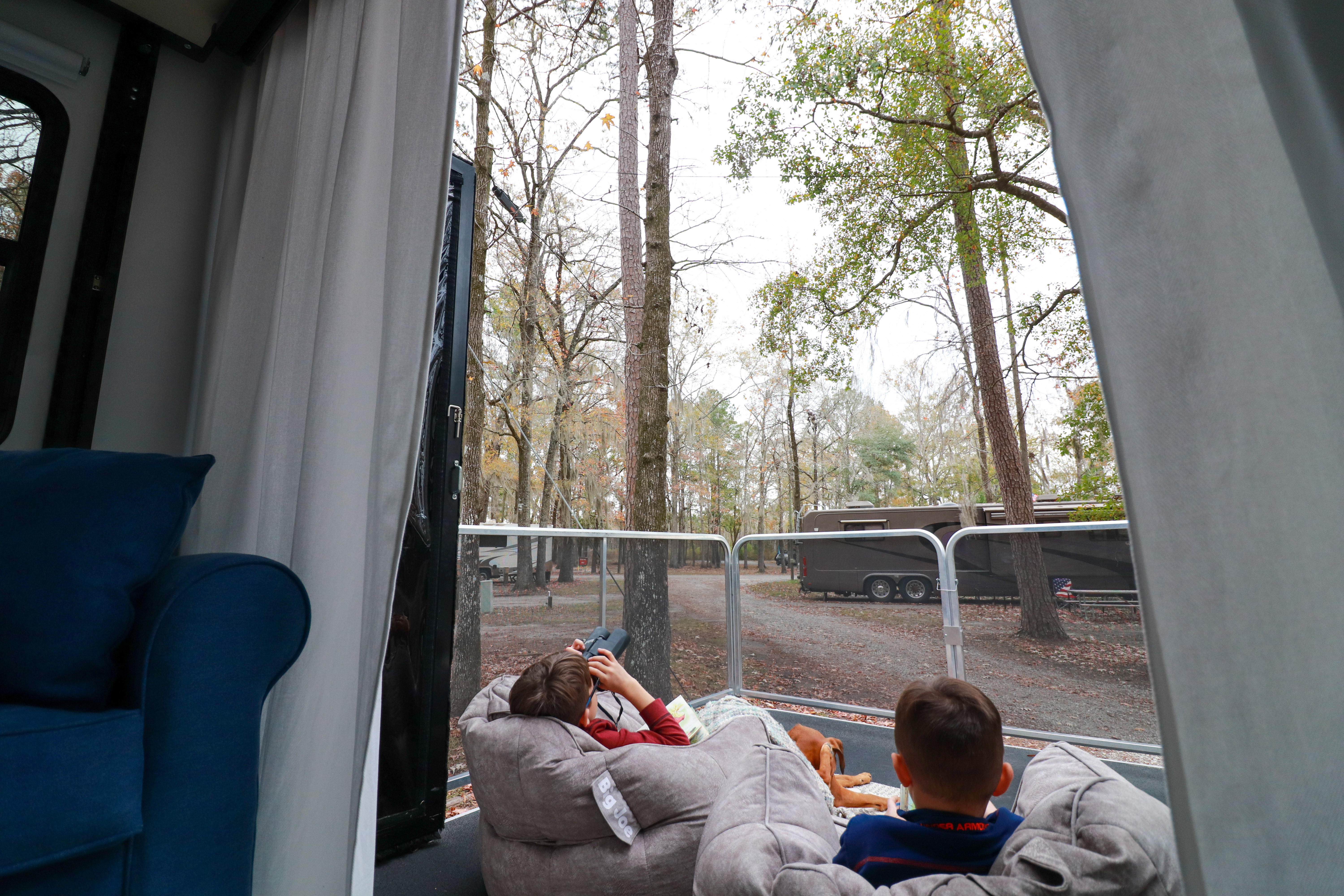 Two young boys sitting in beanbag chairs on an RV patio, looking at the trees around them. 