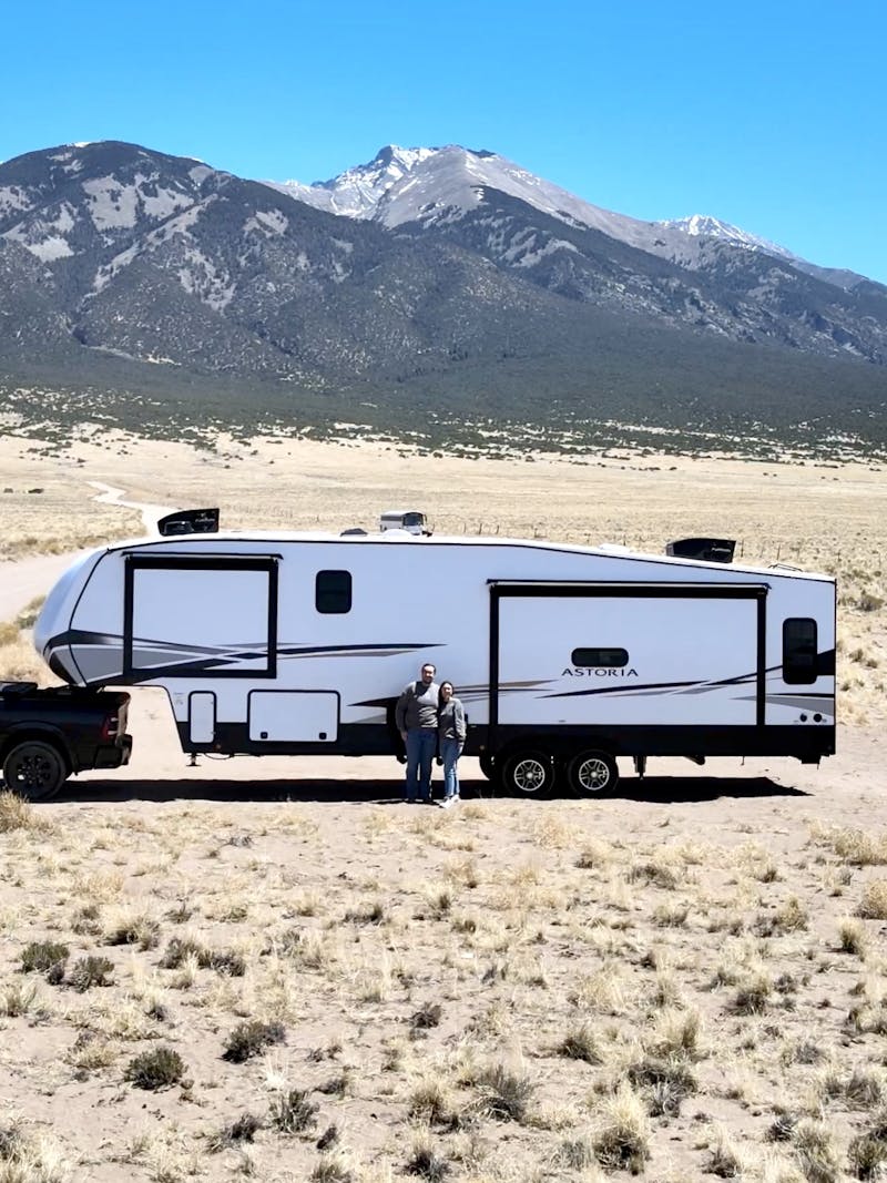 Bailey and Nicole Damberg standing in front of their Dutchmen Astoria Fifth wheel in front of mountains 