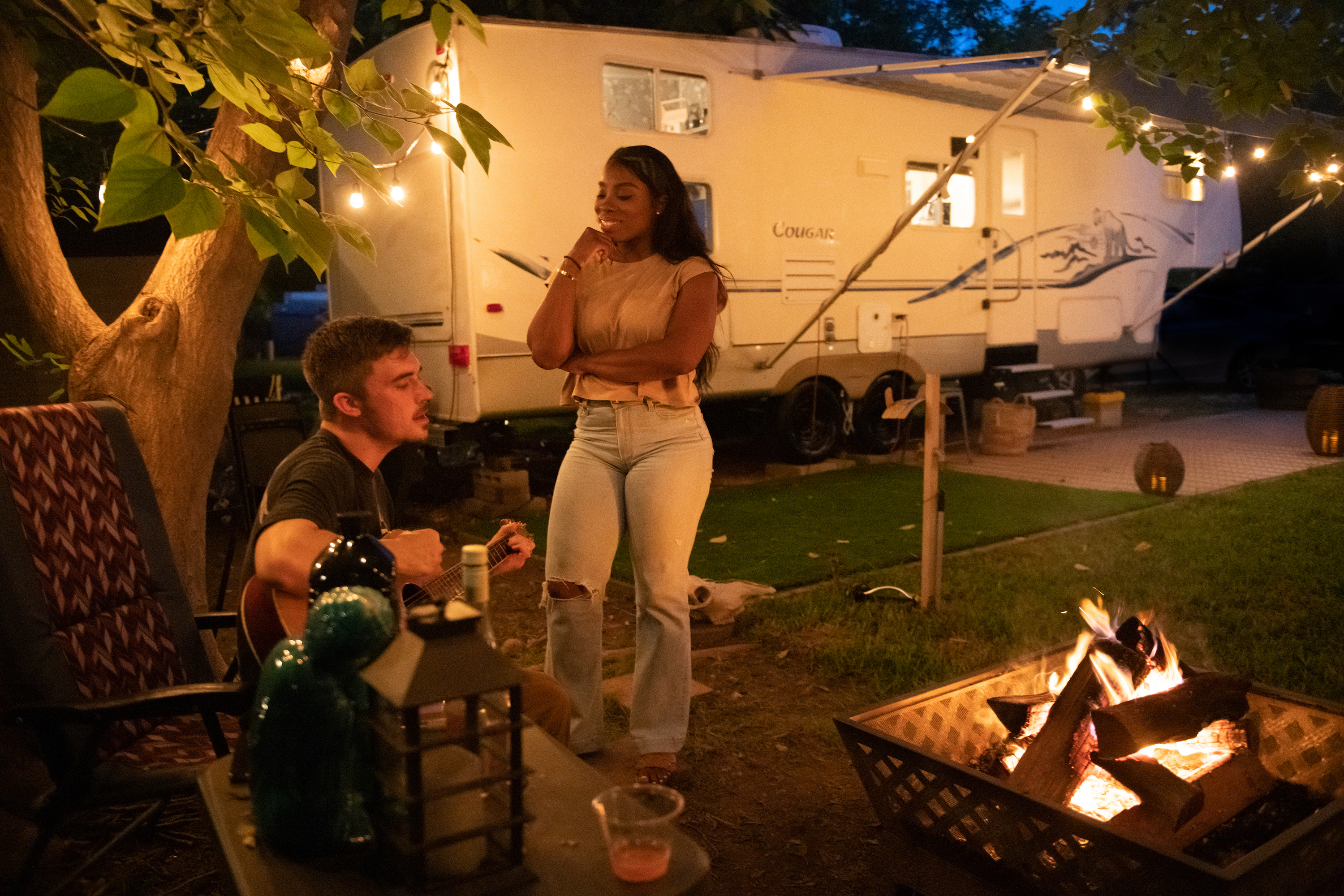 Jessy and Jim singing around a fireplace at night with their Keystone Cougar in the background