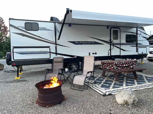 Brandy Gleason's Sundance RV at a camping site with a campfire lit at a safe distance from the RV
