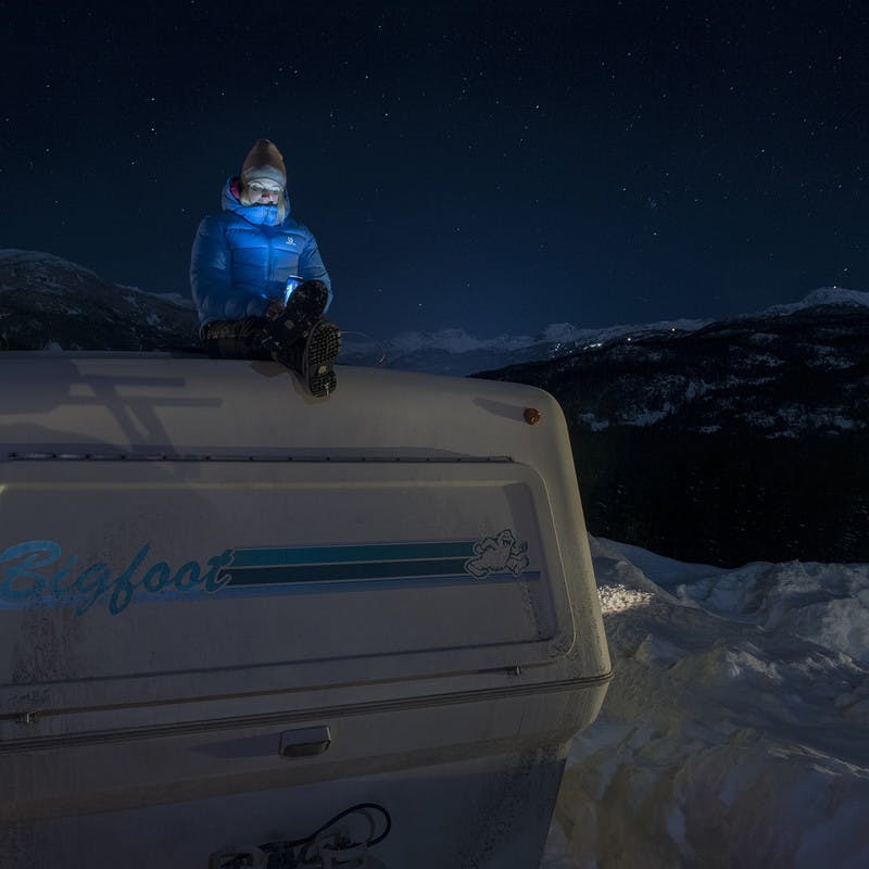 Woman bundled up in a blue winter jacket, winter boots, and winter hat sits on top of her Bigfoot RV.