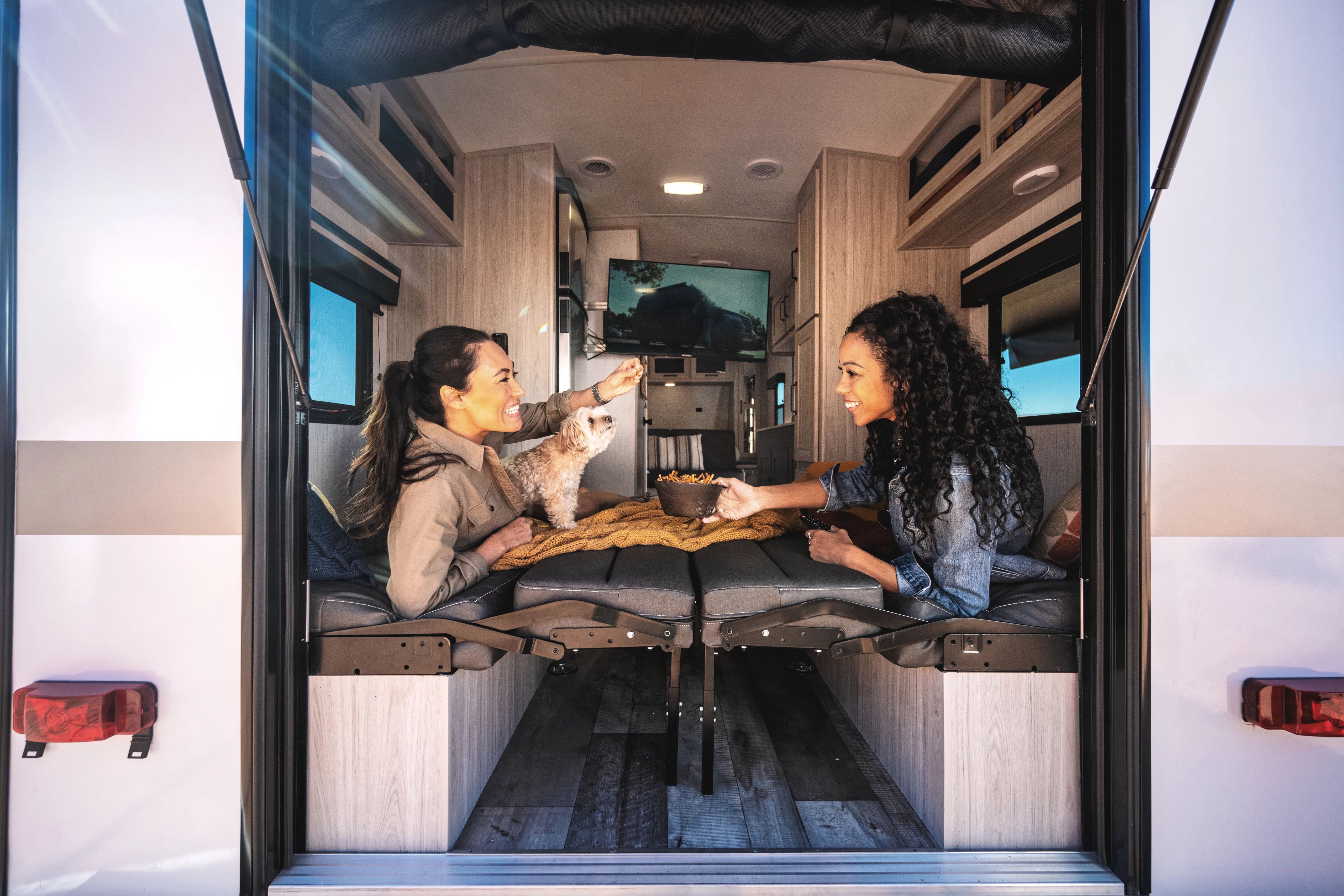 Two women lay on the folding bed of a Heartland Sundance Lightweight Travel Trailer