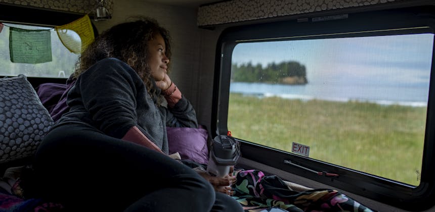 Layla laying in the bed of a Tiffin Wayfarer rv looking out of the window at an ocean