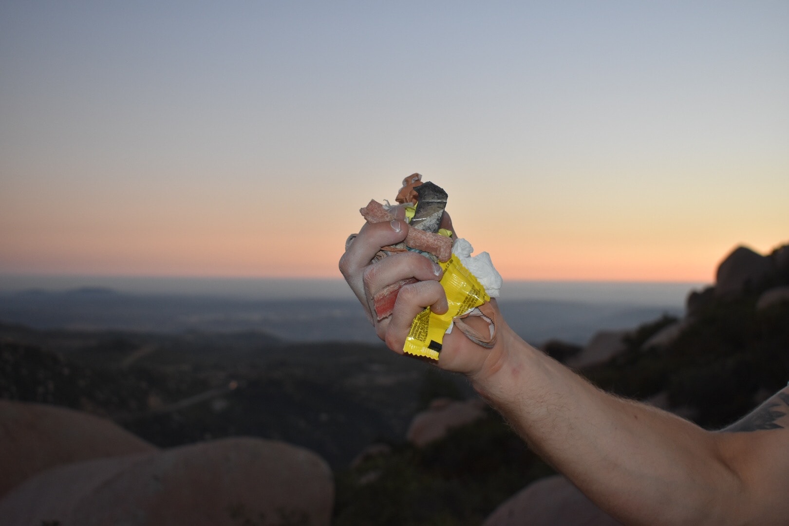 Male hand holding up fistful of trash in front of a sunset