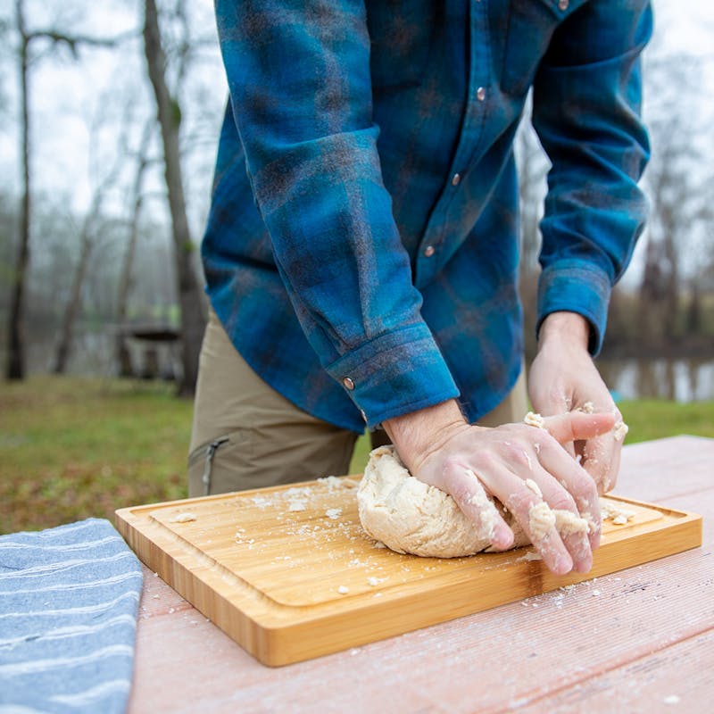 Kneading dough on a cutting board outside.