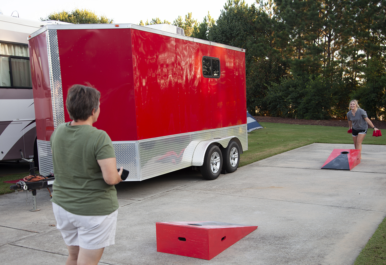 A mother and grown daughter playing cornhole on a paved lot. 