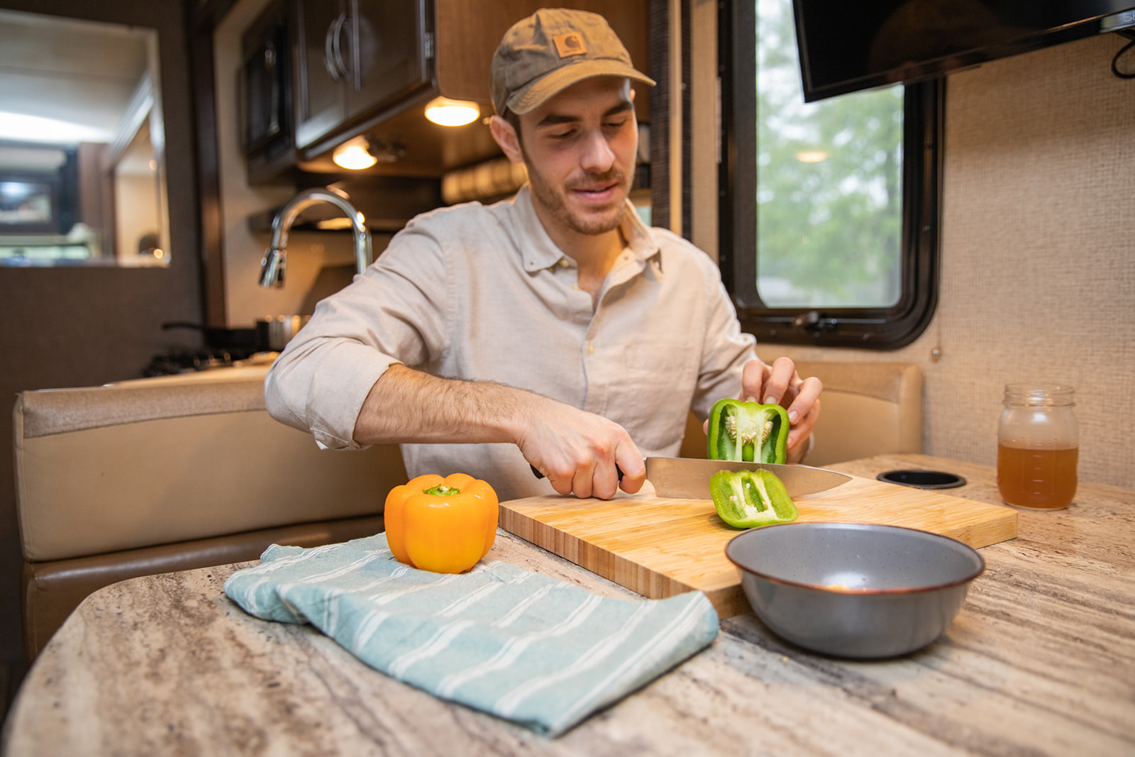 A man cutting a green pepper at an RV kitchen table.