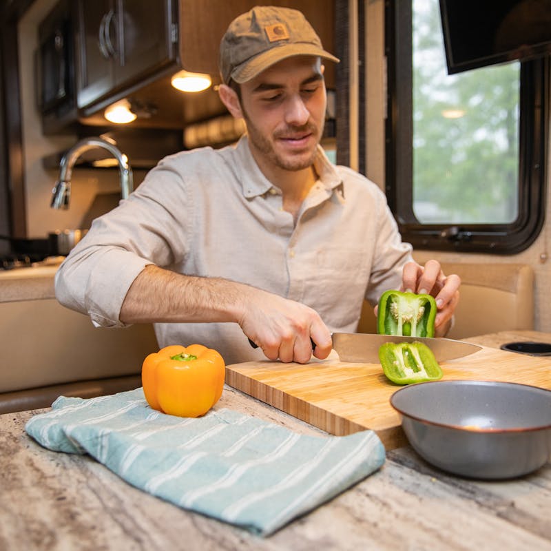 A man cutting a green pepper at an RV kitchen table.