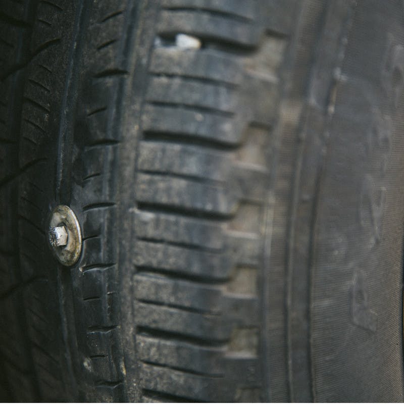 A close-up picture of a car tire with a bolt lodged into it.