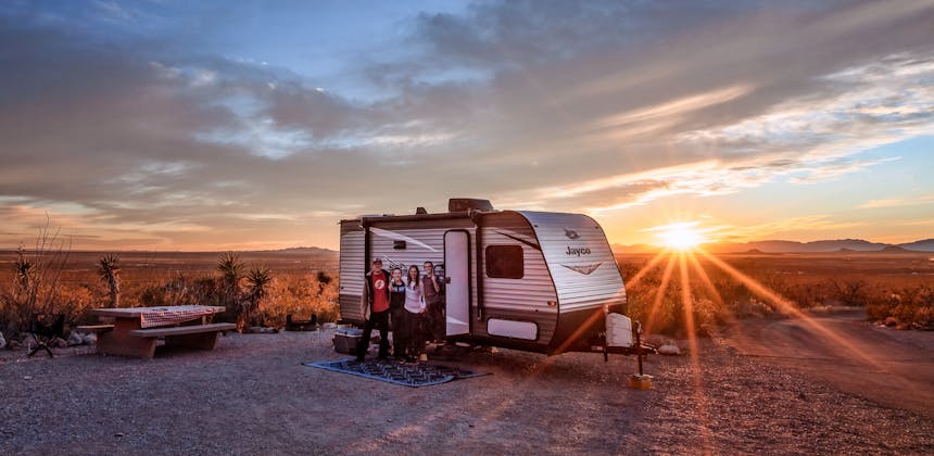 Alison and Jason Takacs pose for a photo in front of their RV with the sun setting behind them