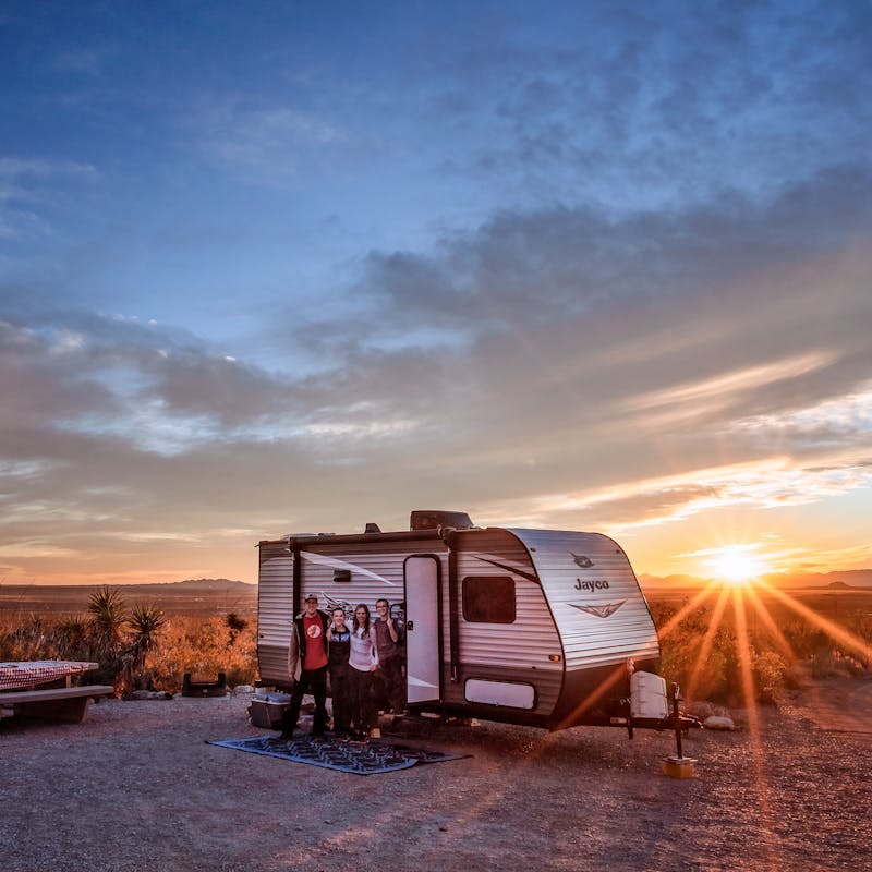 Alison and Jason Takacs pose for a photo in front of their RV with the sun setting behind them