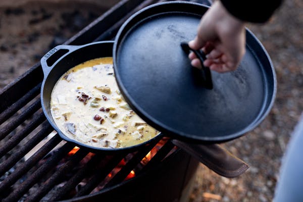 Campfire bacon artichoke frittata being cooked over a fire in a pan.