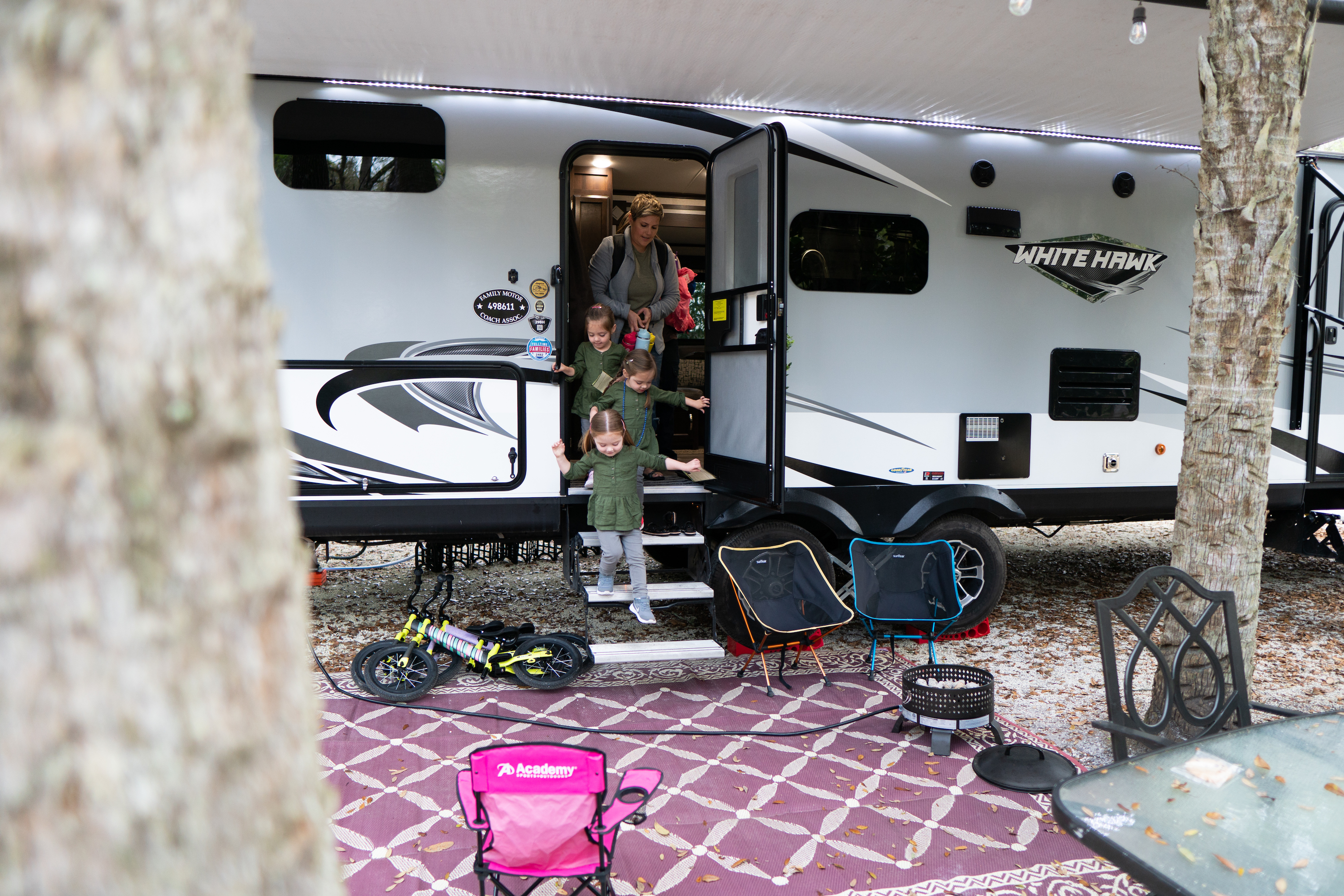 Three girls coming out of an RV with their mom behind them. 