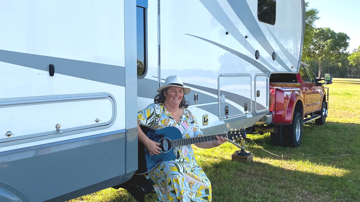 Kimberly Graham playing guitar on the staris of her RV at the Grey Fox Bluegrass Festival
