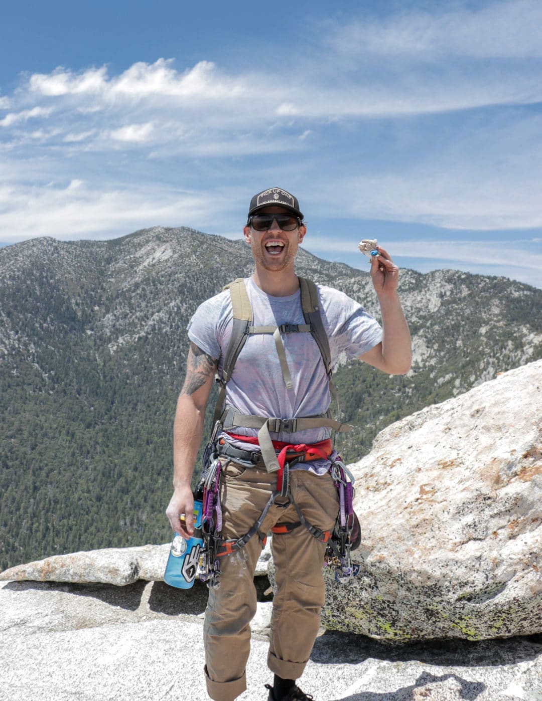 Male rock climber standing on top of mountain, smiling, holding trash