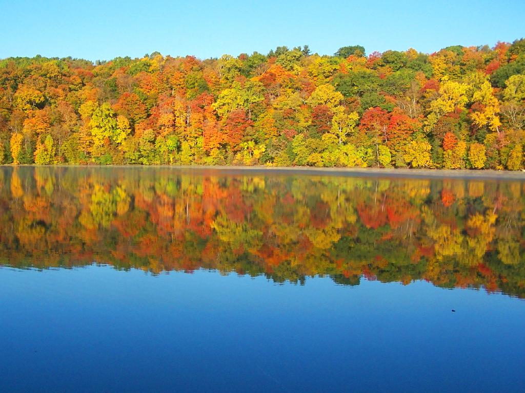 Orange, yellow and red fall trees reflecting on glassy lack in Green Lakes State Park