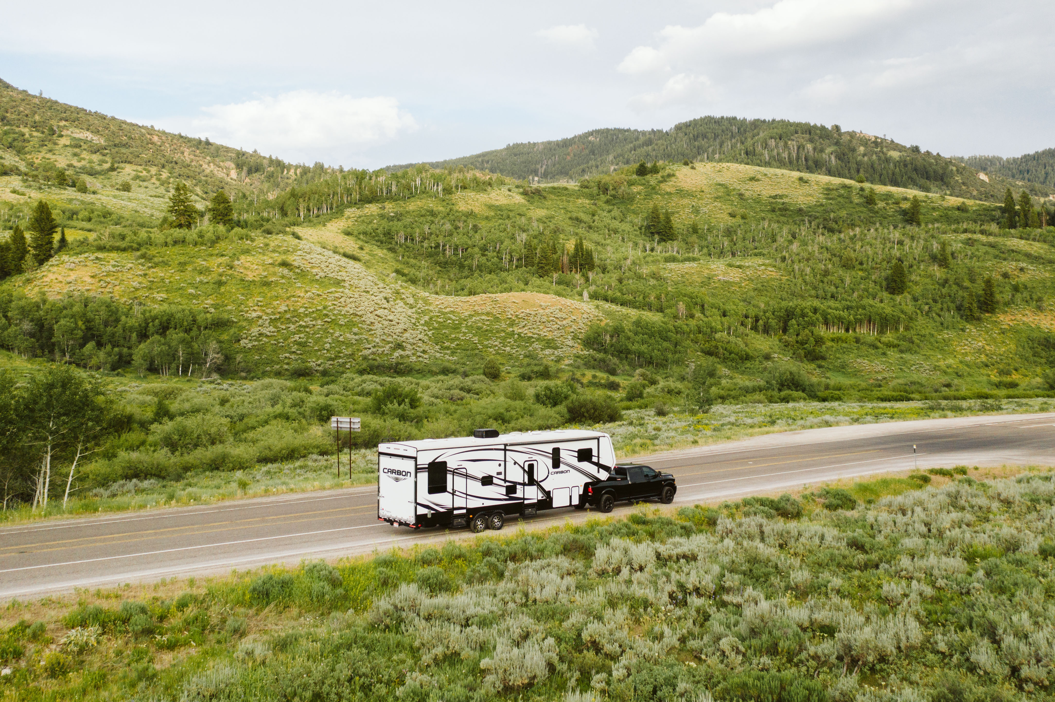 A fifth wheel toy hauler RV driving down a scenic road.