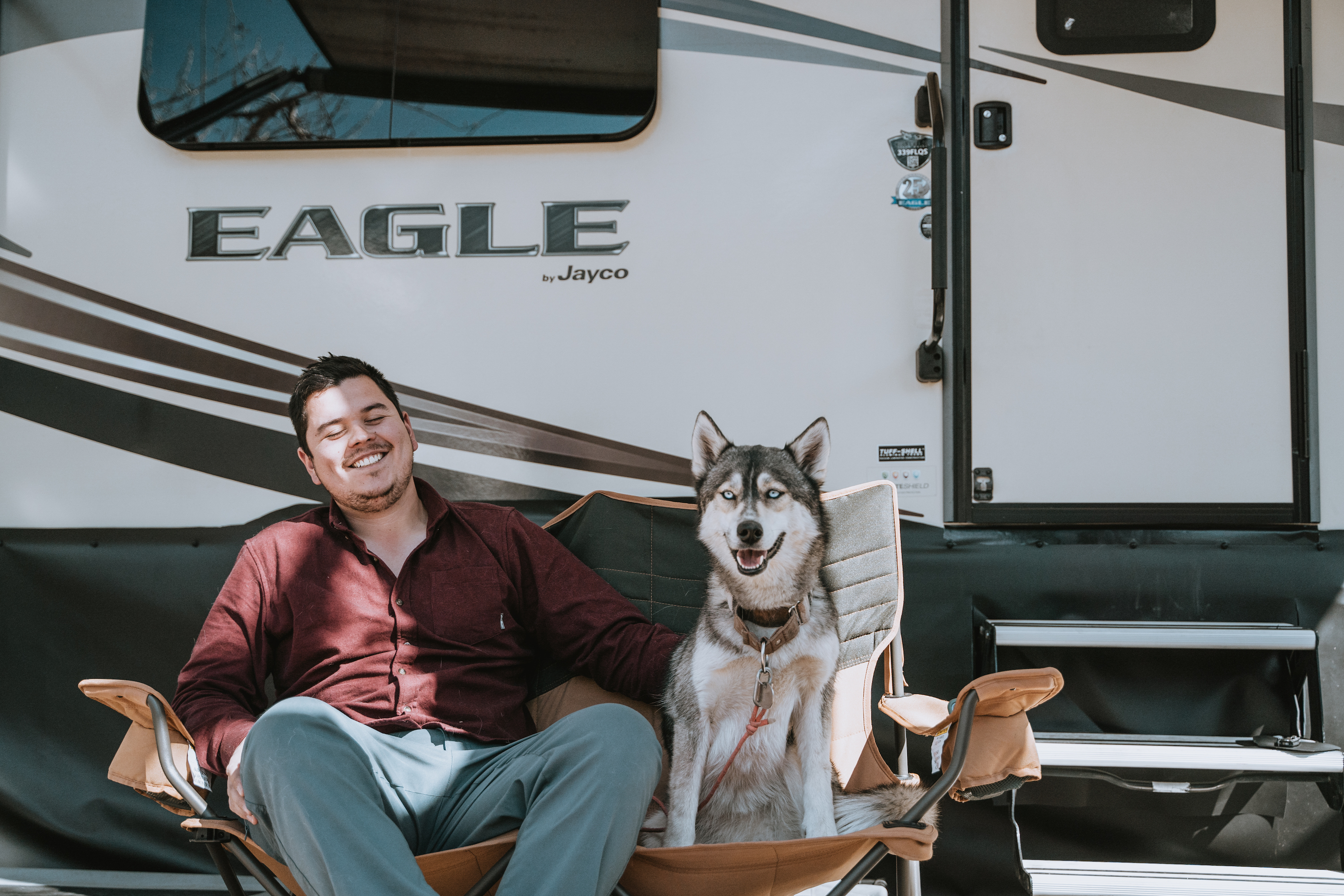 Nico sitting outside the RV with a husky in the chair next to him. 