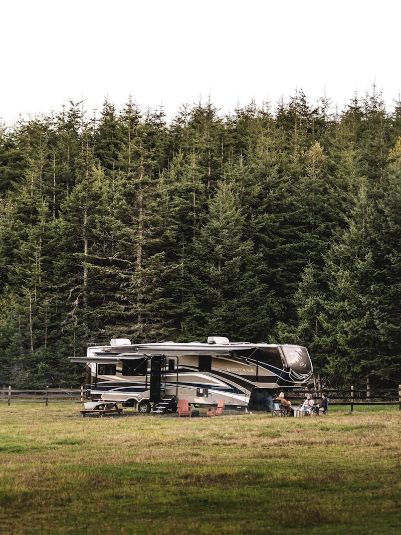 A fifth wheel RV parked in a field with a horse grazing nearby