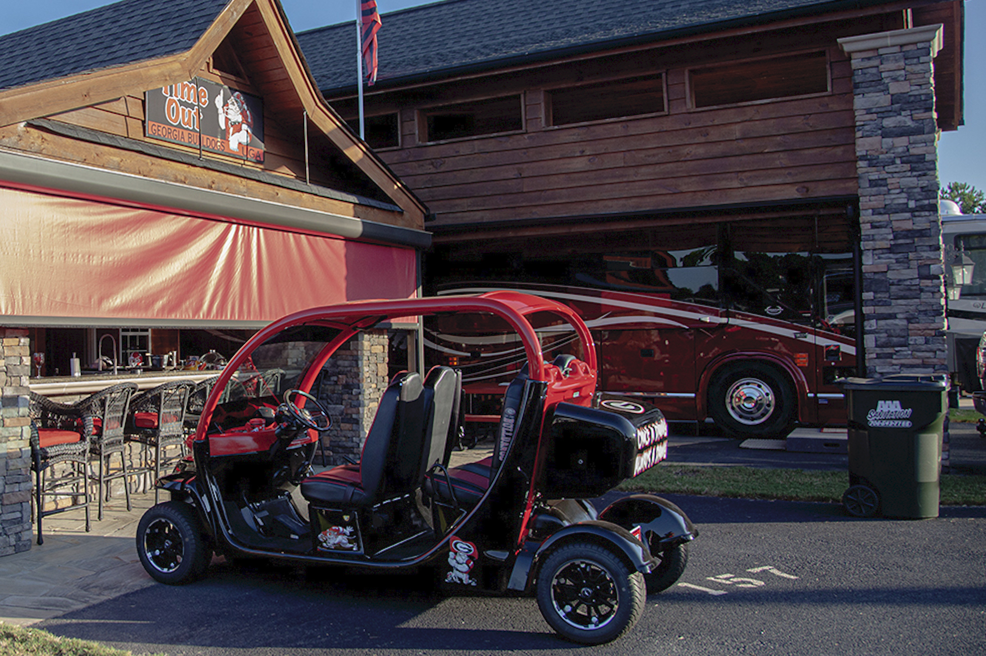 The same tricked-out fancy golf cart parked in front of an elaborate permanent structure at the RV tailgating park. 