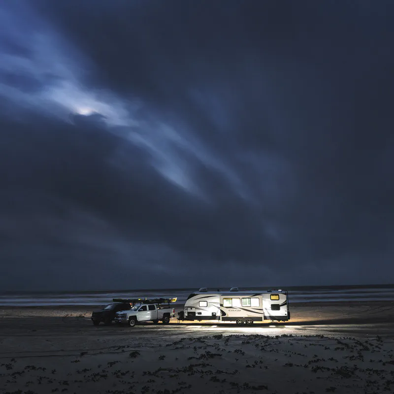 A Keystone Cougar travel trailer RV sits on the beach at nighttime. 