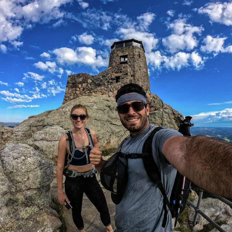 Jesse and Mel on top of a mountain with blue skies all around.