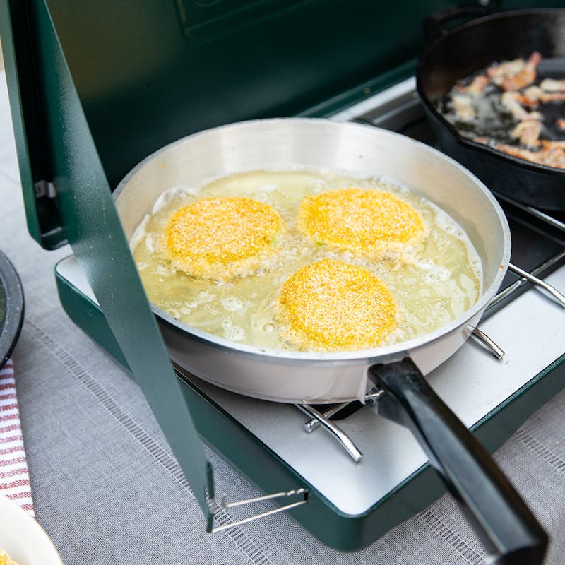 Green tomatoes frying in a pan.