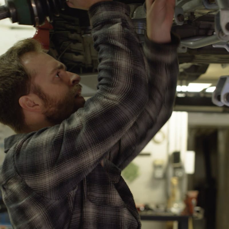 Man in a plaid shirt installing rear axle on a racecar.