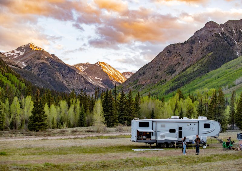 The Carew family standing outside of their RV in front of a sunset and mountain landscape