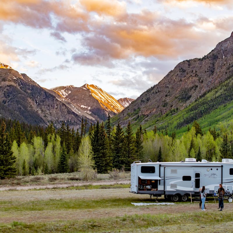 The Carew family standing outside of their RV in front of a sunset and mountain landscape