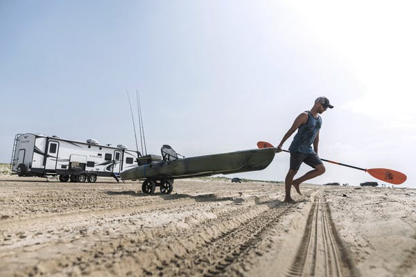 Robert Fields pulls his kayak across a sandy beach that he's unloaded from this Cougar travel trailer. 