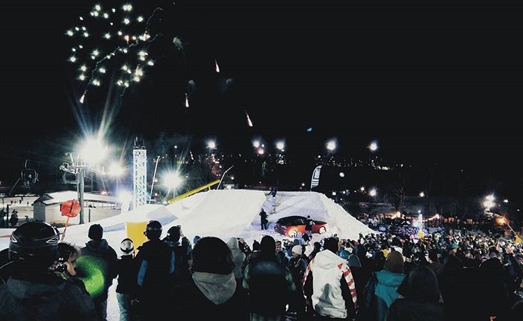 A ski jump at night time with fireworks going off in the background. 