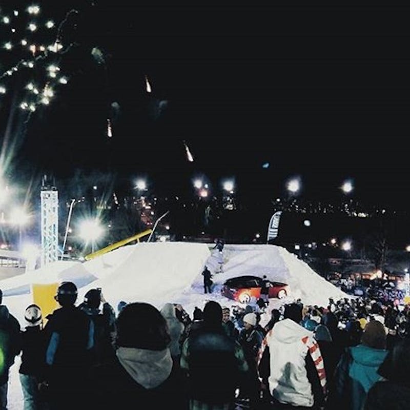 A ski jump at night time with fireworks going off in the background.