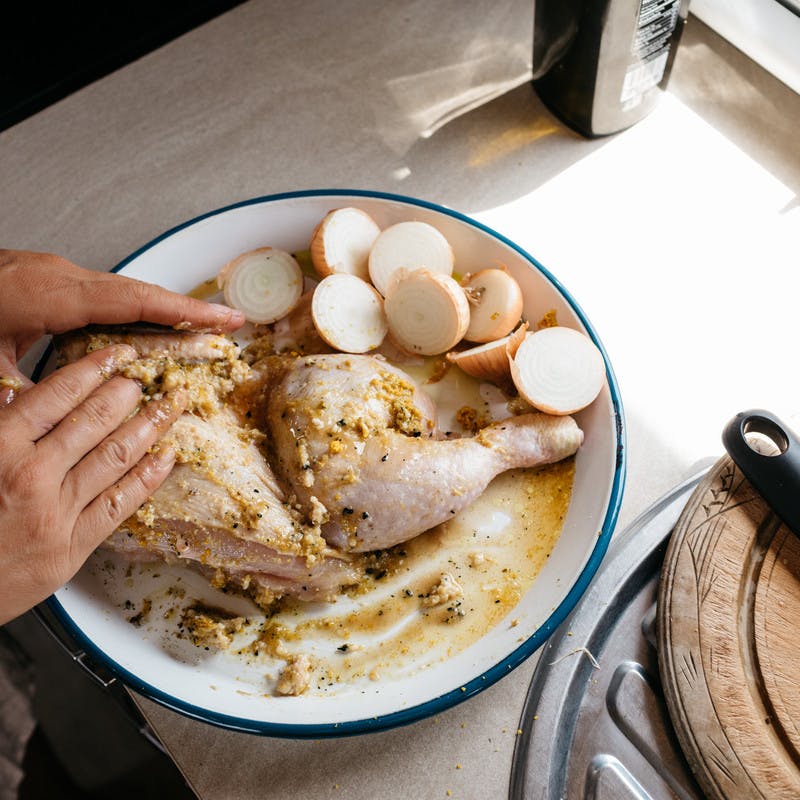 Hands rubbing marinade on raw chicken in a bowl.